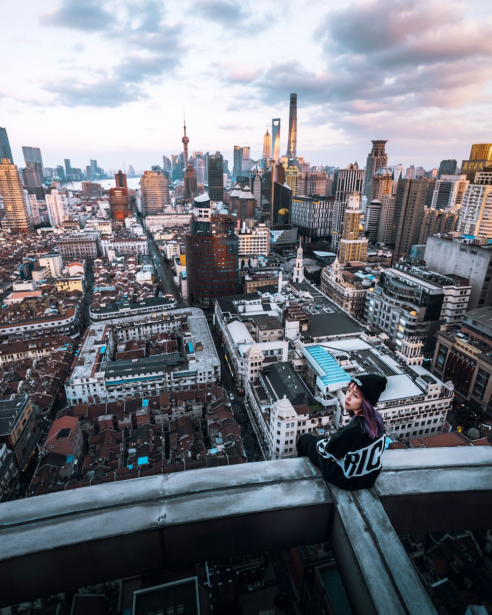 woman sitting on rooftop looking backward overlooking city