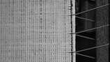 A close-up view of a woven textile, showcasing intricate patterns and textures. Parallel lines and crisscrossed threads create a structured and repetitive design.