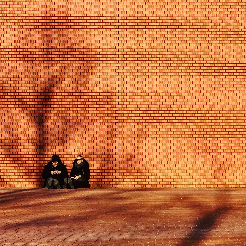 man and woman in black coat sitting against brown wall