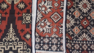 Intricate textile patterns featuring geometric and symmetrical designs in rich colors, showcasing detailed motifs common in traditional fabric. The repeating shapes and lines are crafted with precision, creating a visually captivating and culturally significant piece.