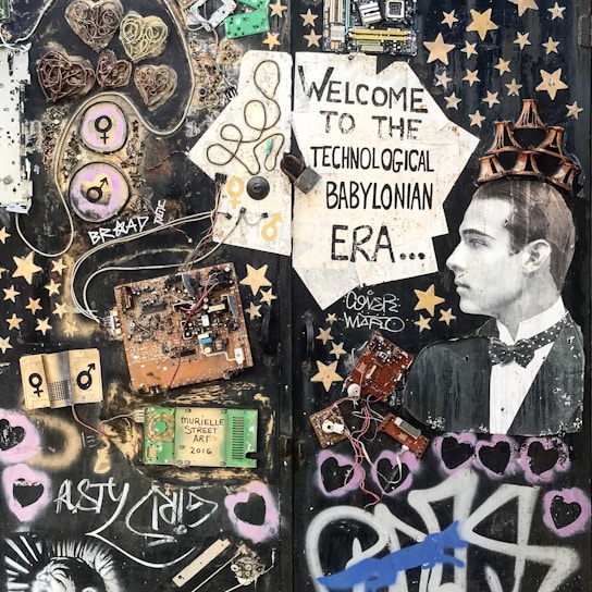 A collage featuring various electronic components, wires, and circuit boards arranged artistically on a dark background. A vintage photograph of a man wearing a tuxedo is incorporated into the scene, positioned to the right, with a cardboard crown on his head. The composition includes stenciled graphics, stars, hearts, and graffiti art, with text that reads 'Welcome to the Technological Babylonian Era'.