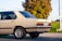 A beige vintage sedan is parked on a paved surface with a lush green landscape and a tree in the background. The car features a distinctive chrome trim, classic styling, and European license plate.