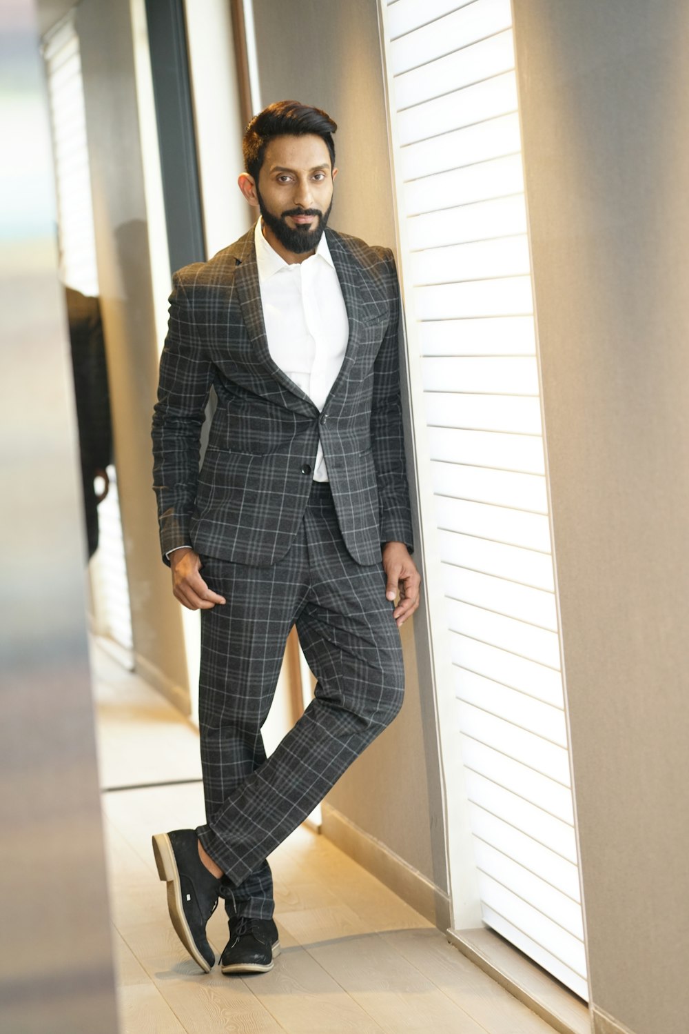 man in gray and white plaid suit jacket standing beside wall