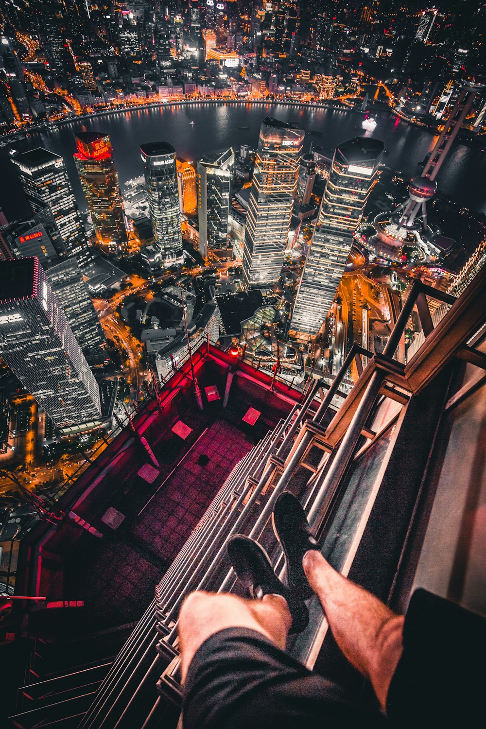 person standing on edge of building with highrised lighted buildings near river during night time