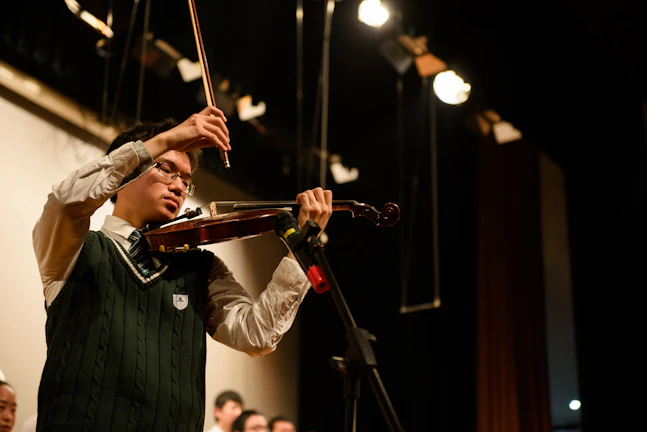 A young violinist concentrating deeply during a Crescendo Academy recital under warm stage lights.