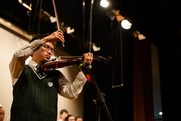 A violinist passionately playing on stage under warm spotlight.