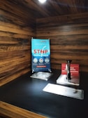 A wooden counter top is equipped with a sauce dispenser and a small ice container. A sign on the wall advocates stopping the use of plastic straws, showing a crossed-out straw. Another nearby sign reminds patrons to take only the necessary amount of sauce.