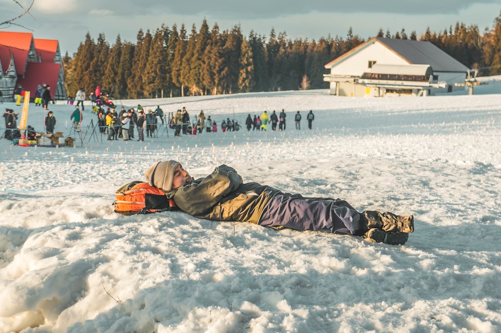 person lying on snow using his bag as pillow