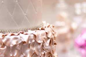 Close-up of a beautifully decorated custom cake with pink and gold accents on a white pearl tablecloth.