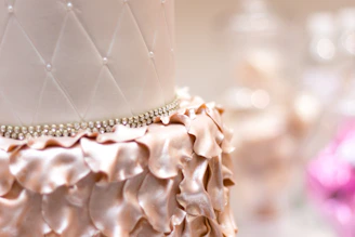 Close-up of a beautifully decorated custom cake with pink and gold accents on a white pearl tablecloth.