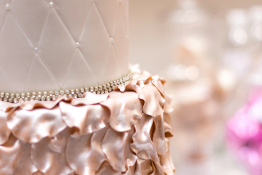 Close-up of a beautifully decorated pink and gold cake with delicate floral details on a white pearl background.