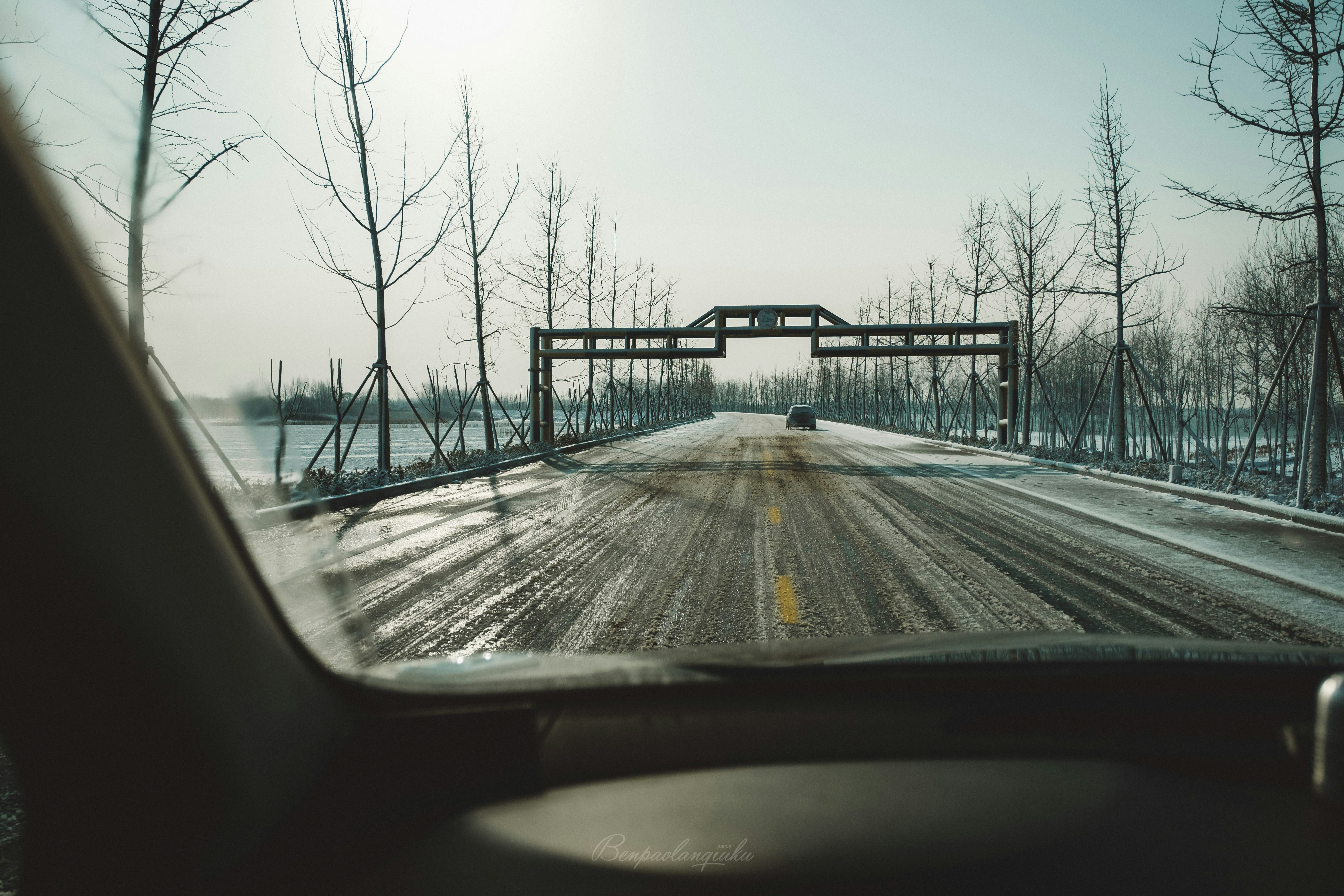 black car on straight road bridge under white sky