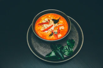 A glowing neon-lit plate of Tom Yum soup garnished with fresh herbs and chili slices.