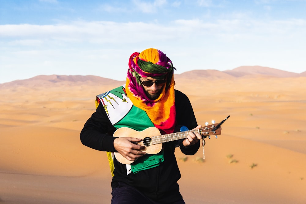 man in turban playing ukulele on desert