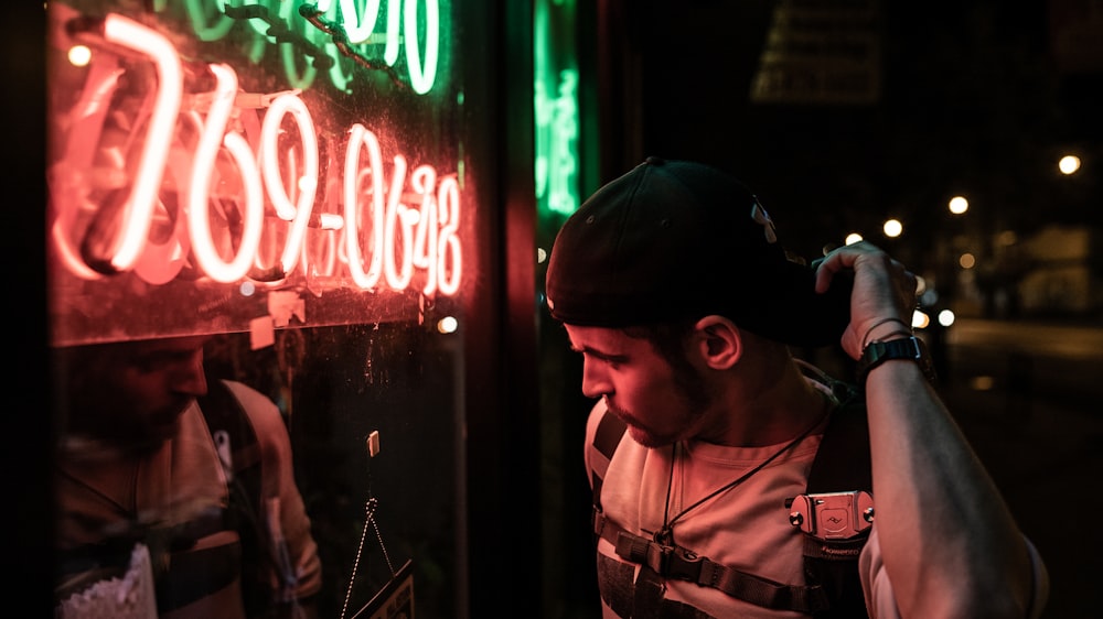 man in white crew-neck shirt holding fitted cap standing in front of LED 769-0648 light signage