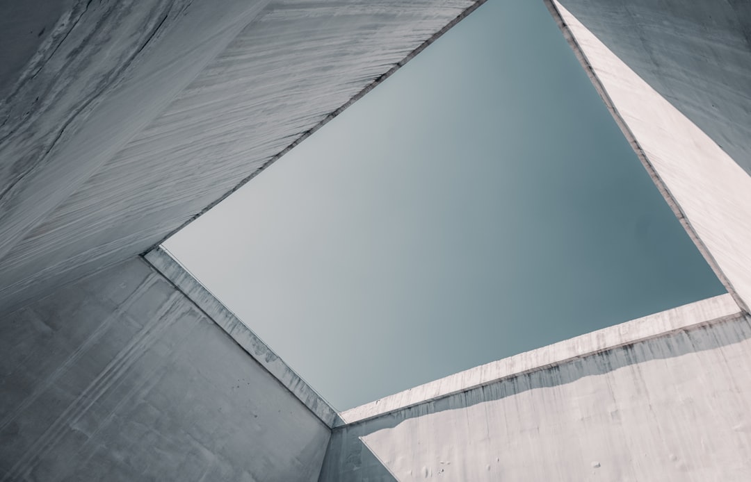 low angle photography of grey concrete walls under white and blue sky