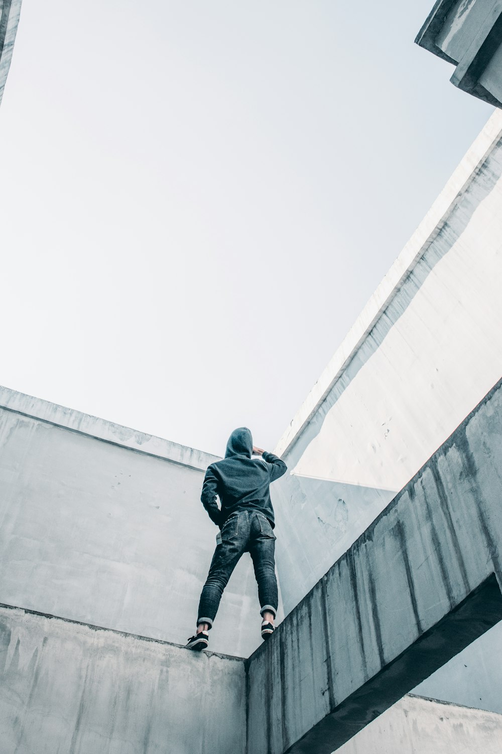 person wearing hoodie and blue denim jeans standing near grey concrete wall during daytime