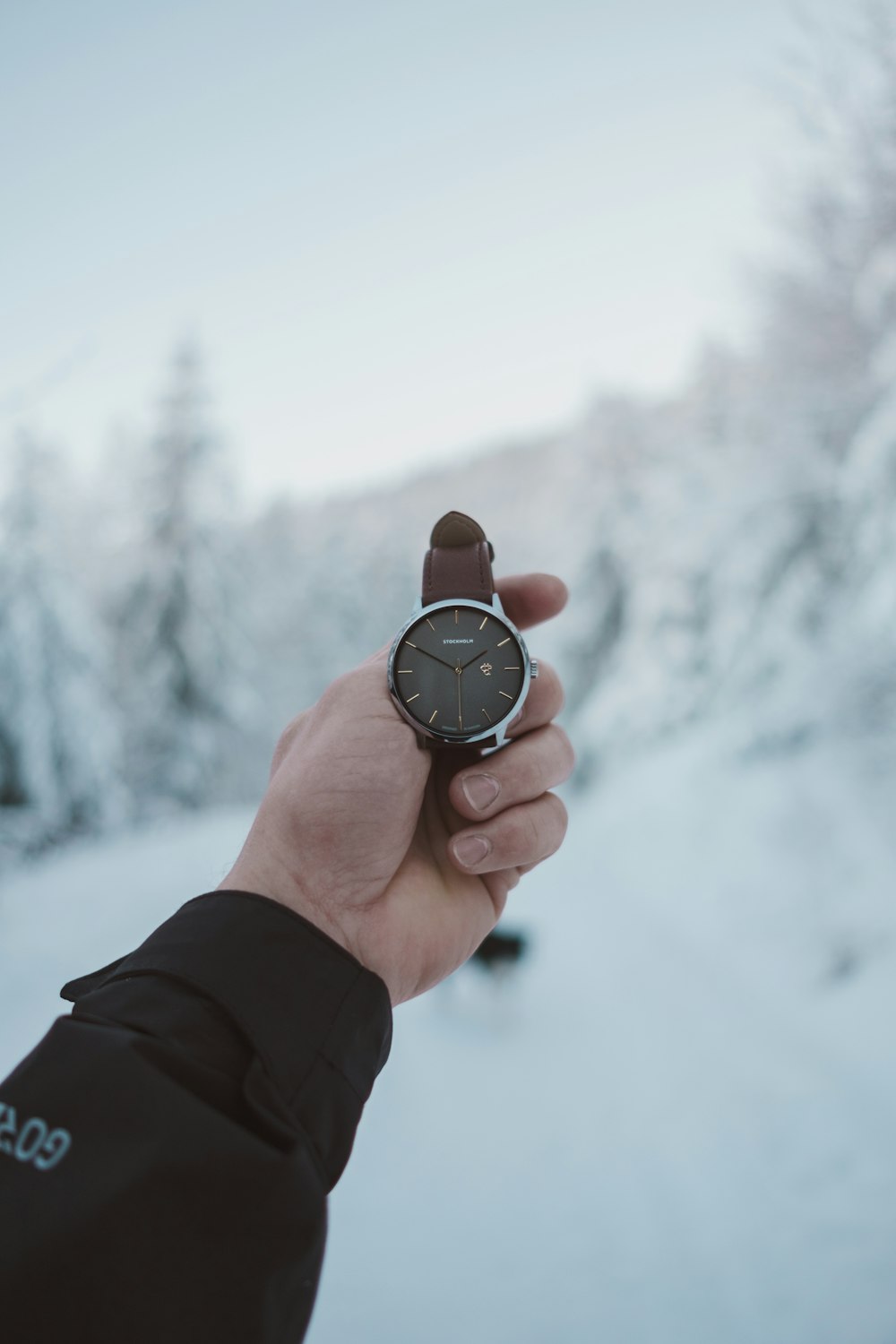 person holding round silver-colored analog watch with brown leather band at 2:50