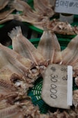 Several dried fish are arranged on a green tray with a price tag displaying 30,000 written in a non-Latin script. The fish have their tails prominently displayed, showing detailed textures in their dried state.