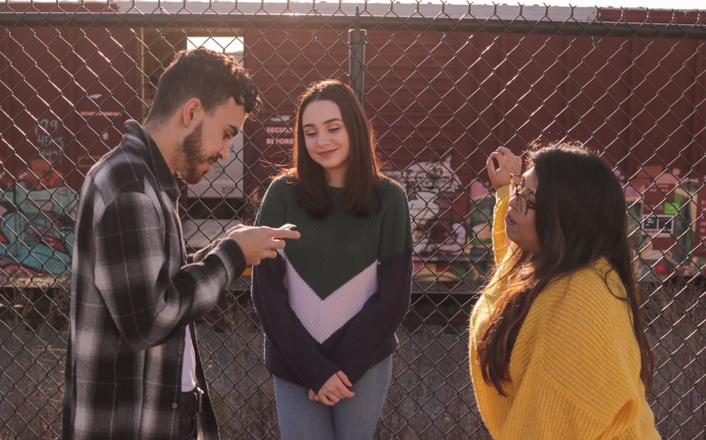 two women and one man standing near fence