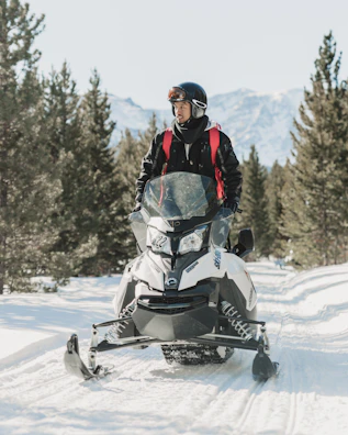 man in black winter jacket driving white snowmobile on snow-covered ground during daytime