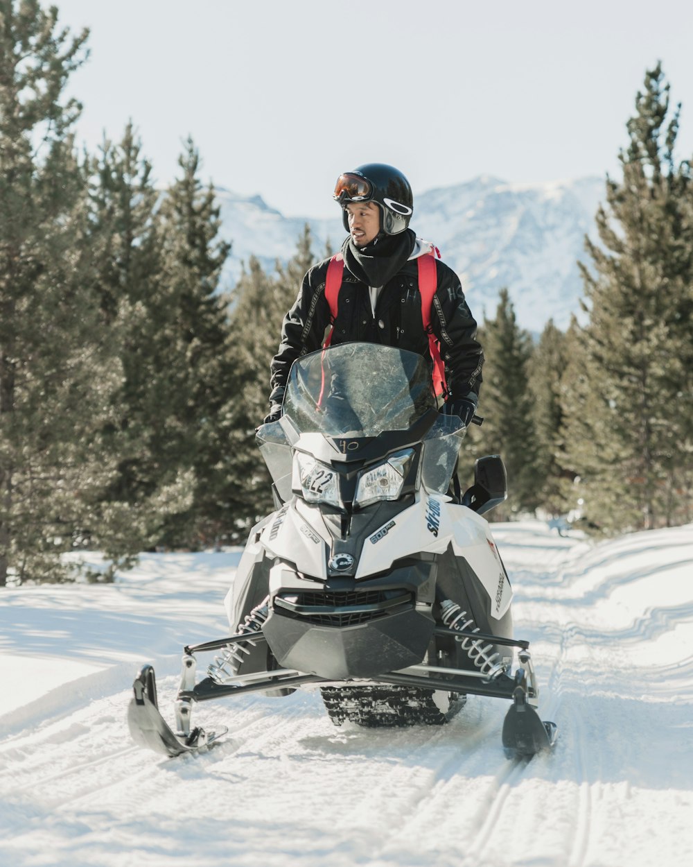 hombre con chaqueta de invierno negra conduciendo una moto de nieve blanca en un terreno cubierto de nieve durante el día