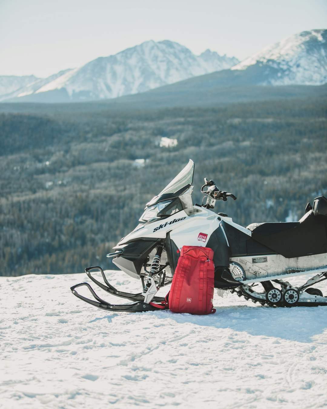white and black snowmobile with red backpack on top of mountain
