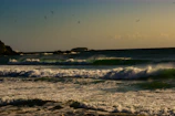 Surfers catching waves on a breezy day along a sandy Atlantic beach.