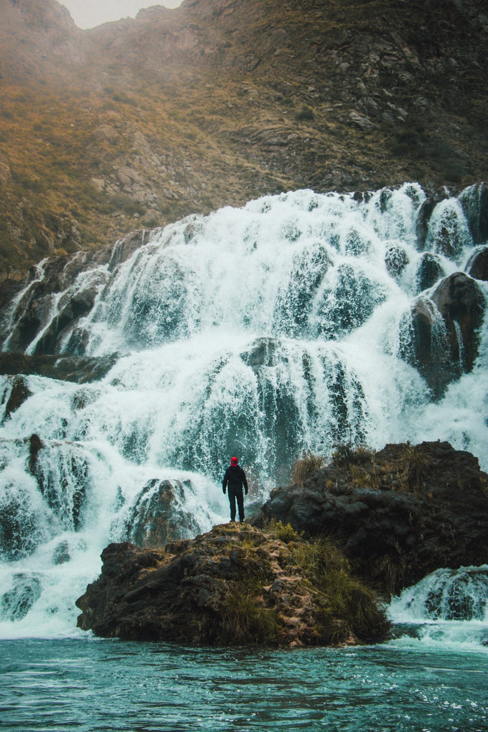 man standing on rock in front of waterfall