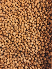A close-up view of a large pile of hazelnuts with their brown shells intact. The image is densely packed with nuts, showing the texture and natural patterns on the shells.