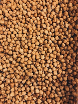 A close-up view of a large pile of hazelnuts with their brown shells intact. The image is densely packed with nuts, showing the texture and natural patterns on the shells.