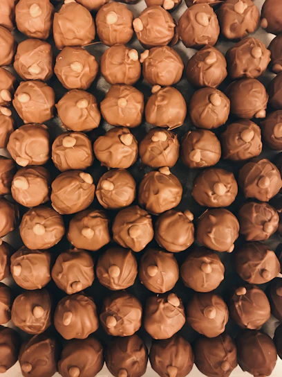 Close-up of rich, glossy chocolates arranged artistically on a dark plate with a hint of cocoa powder dusted around.