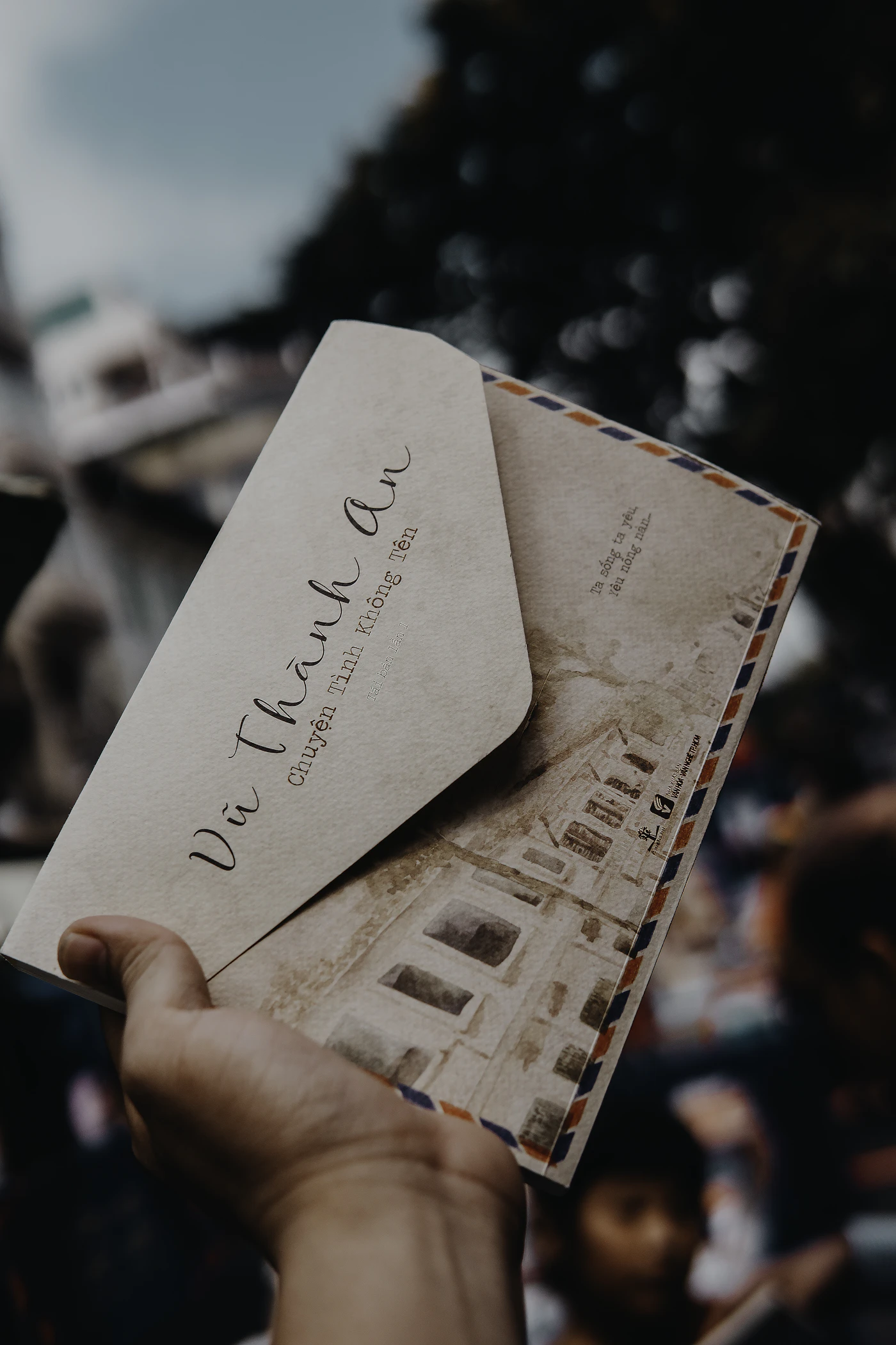 A hand holding a sealed handwritten letter and its envelope outdoors