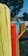 A colorful wooden fence with brightly painted vertical planks in yellow, red, blue, and green. The fence is in an outdoor setting with trees in the background and sections of a playground or park visible.