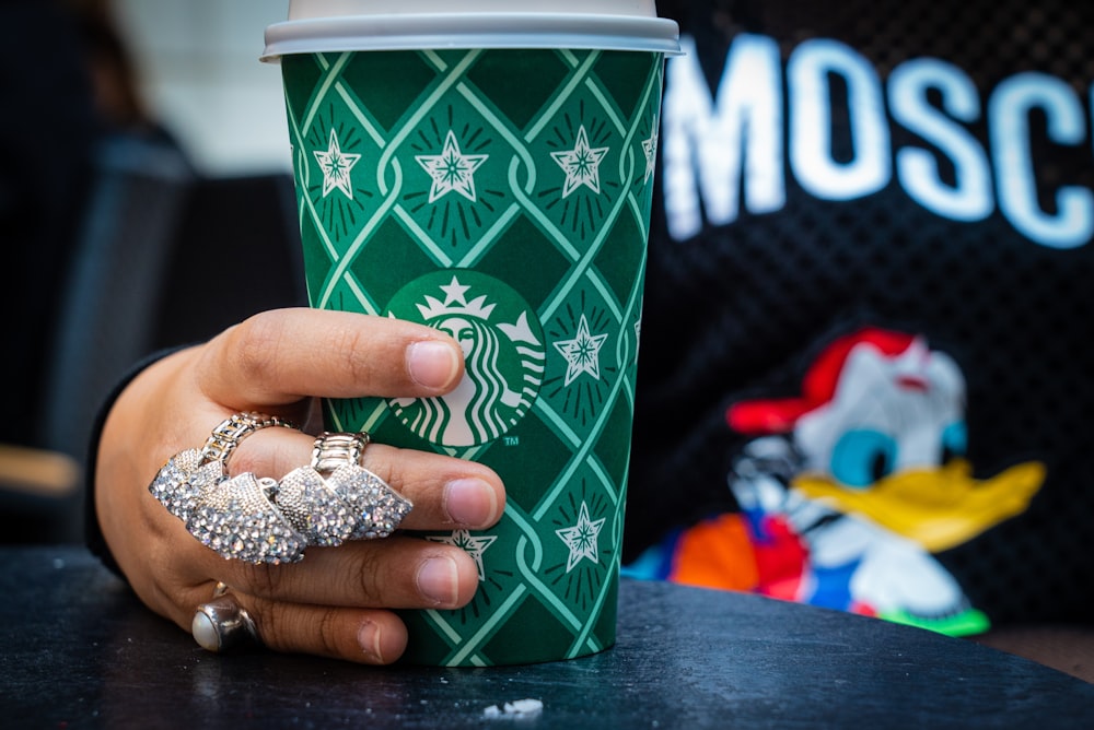 green Starbucks coffee cup held by hand with multiple rings