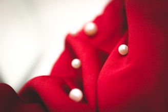 Rich red fabric features several large, glossy white pearls embedded within its softly draped surface, creating a luxurious and elegant texture.