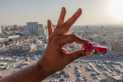 A close-up of a hand holding a miniature car model over financial charts and graphs.