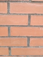 A section of a brick wall with horizontal rows of reddish-orange bricks and gray mortar in between.