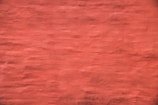 A plain and textured wall painted in a reddish hue, displaying subtle variations in the brush strokes.