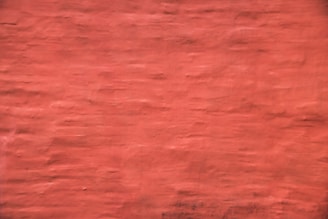 A plain and textured wall painted in a reddish hue, displaying subtle variations in the brush strokes.