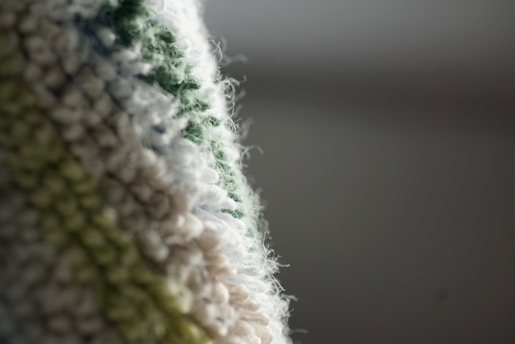 Close-up of a fluffy, textured fabric with a gradient of colors ranging from white to green. The fabric appears to have a soft, fuzzy surface with a weave-like pattern.