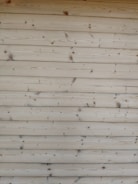 A series of horizontal wooden planks with visible knots and grain patterns. The wood appears freshly cut or possibly sanded, showcasing a natural light brown color.
