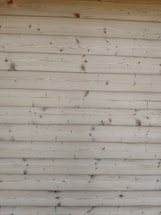 A series of horizontal wooden planks with visible knots and grain patterns. The wood appears freshly cut or possibly sanded, showcasing a natural light brown color.