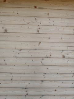 A series of horizontal wooden planks with visible knots and grain patterns. The wood appears freshly cut or possibly sanded, showcasing a natural light brown color.
