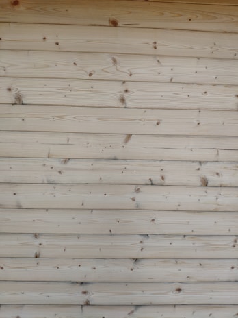 A series of horizontal wooden planks with visible knots and grain patterns. The wood appears freshly cut or possibly sanded, showcasing a natural light brown color.