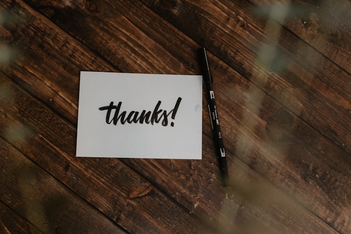 card that says thanks next to a pen on a wooden table
