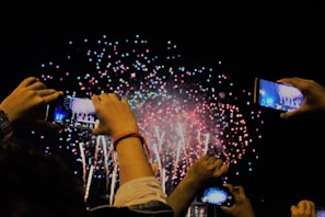 A group selfie of diverse $happy holders smiling wide, fireworks bursting in the background.