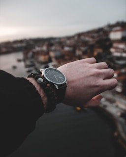 Close-up of a sleek urban watch on a wrist against a cityscape background at sunset