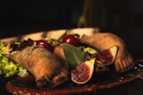 A close-up of a dish featuring two baked pastries creatively shaped like feet, served on a bed of lettuce with cherry tomatoes and sliced figs. The pastries sit on a thick, rustic red sauce.