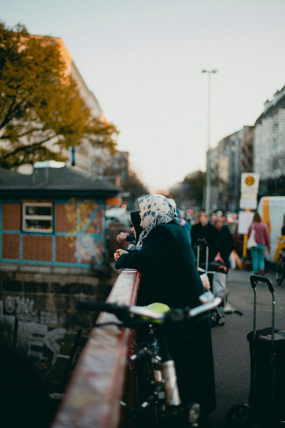 woman wearing black coat leaning on red metal fence during daytime